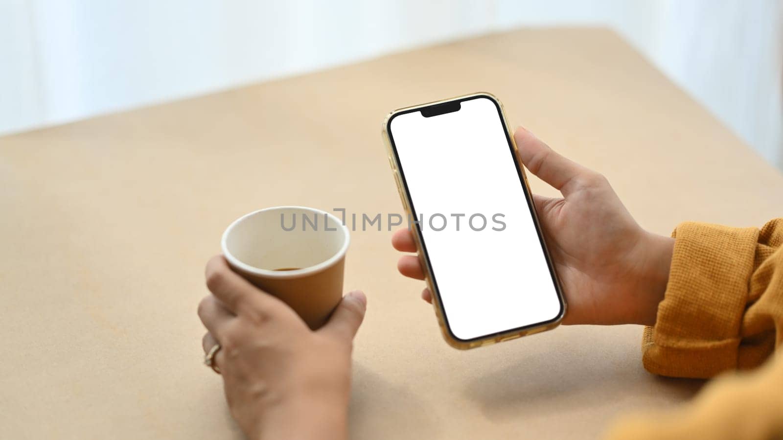 Closeup woman using mobile phone and drinking coffee at desk. Empty screen for advertising or message.