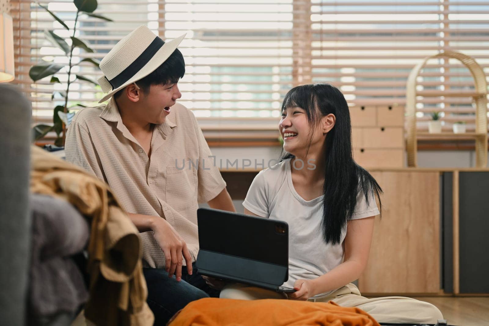 Happy young couple talking cheerfully while packing suitcase for vacations together in living room.