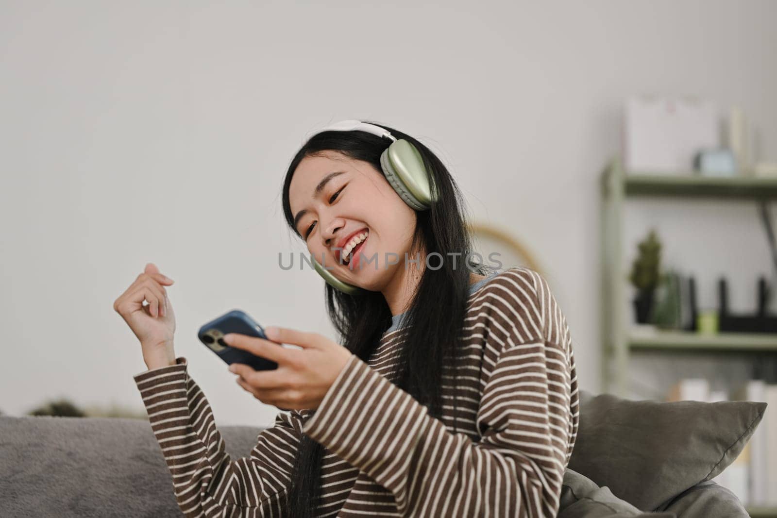 Cheerful young woman enjoying her favorite music playlist, singing and dancing at home.