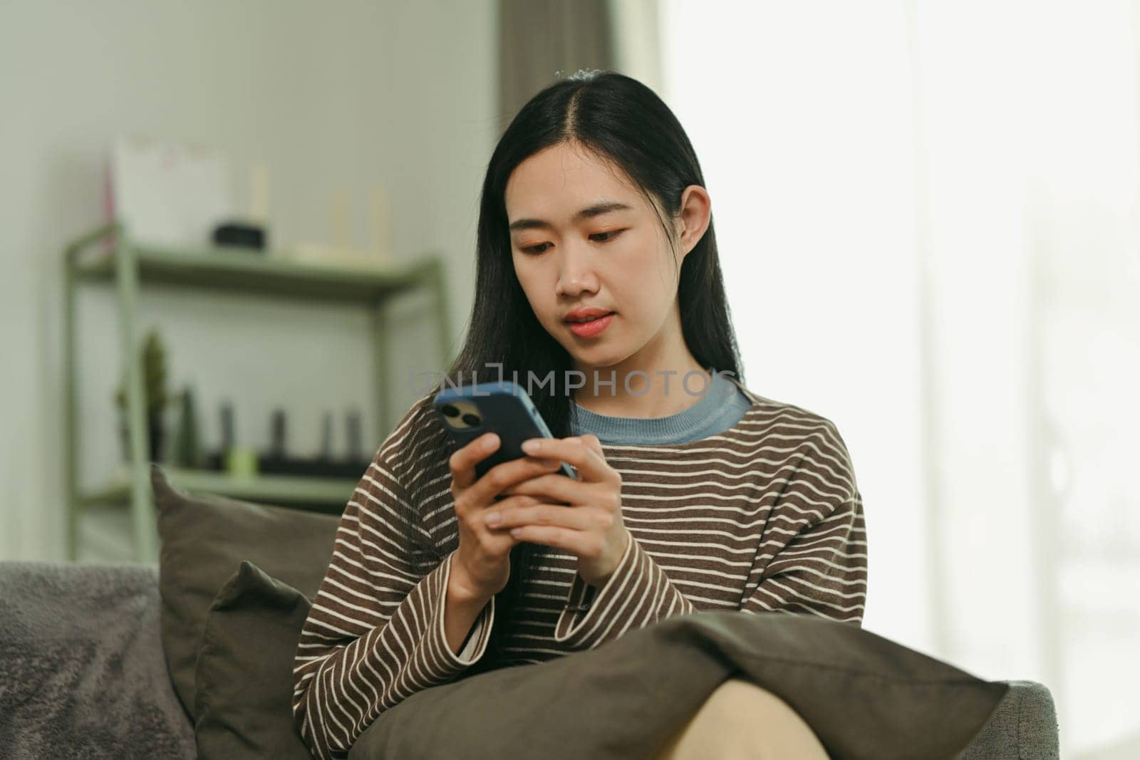 Beautiful young woman relaxing on comfortable sofa while chatting on mobile phone.