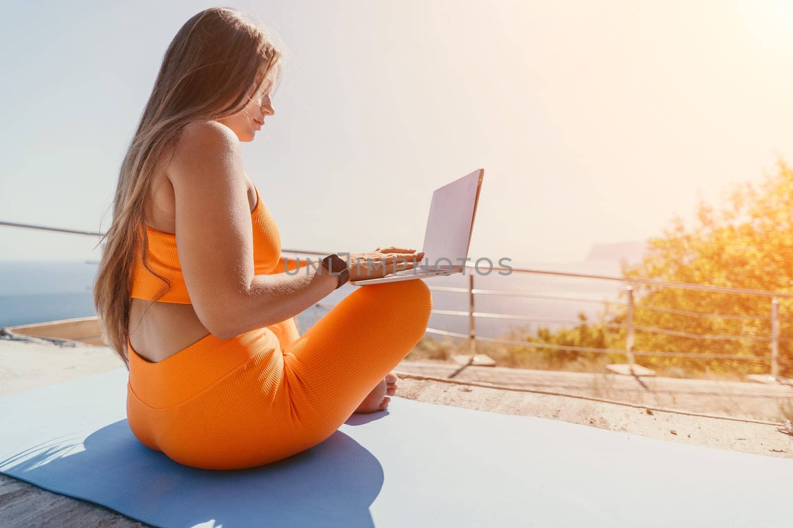 Woman laptop sea. Working remotely on seashore. Happy successful woman female freelancer working on laptop by the sea at sunset, makes a business transaction online. Freelance, remote work on vacation by panophotograph