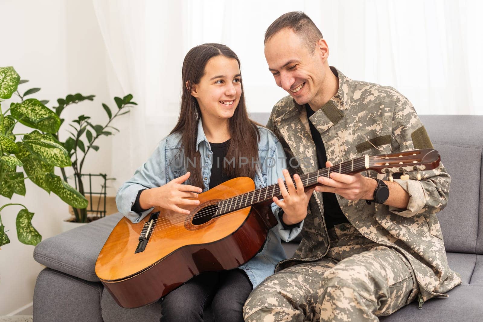 The veteran came back from army. A man in uniform with his daughter. The veteran is playing the guitar. High quality photo