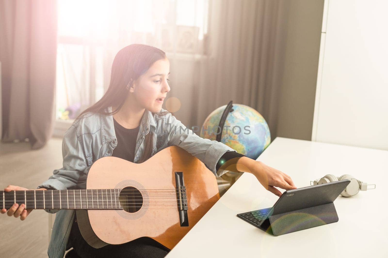 Beautiful young girl with long hair playing the guitar, sitting at home . studying the melody. Home leisure, hobbies, self-development. High quality photo