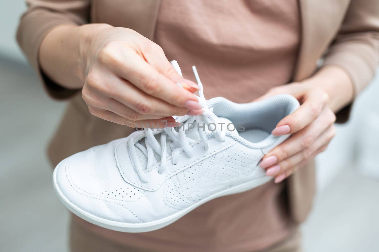 Woman holding stylish sport shoe indoors, closeup. High quality photo