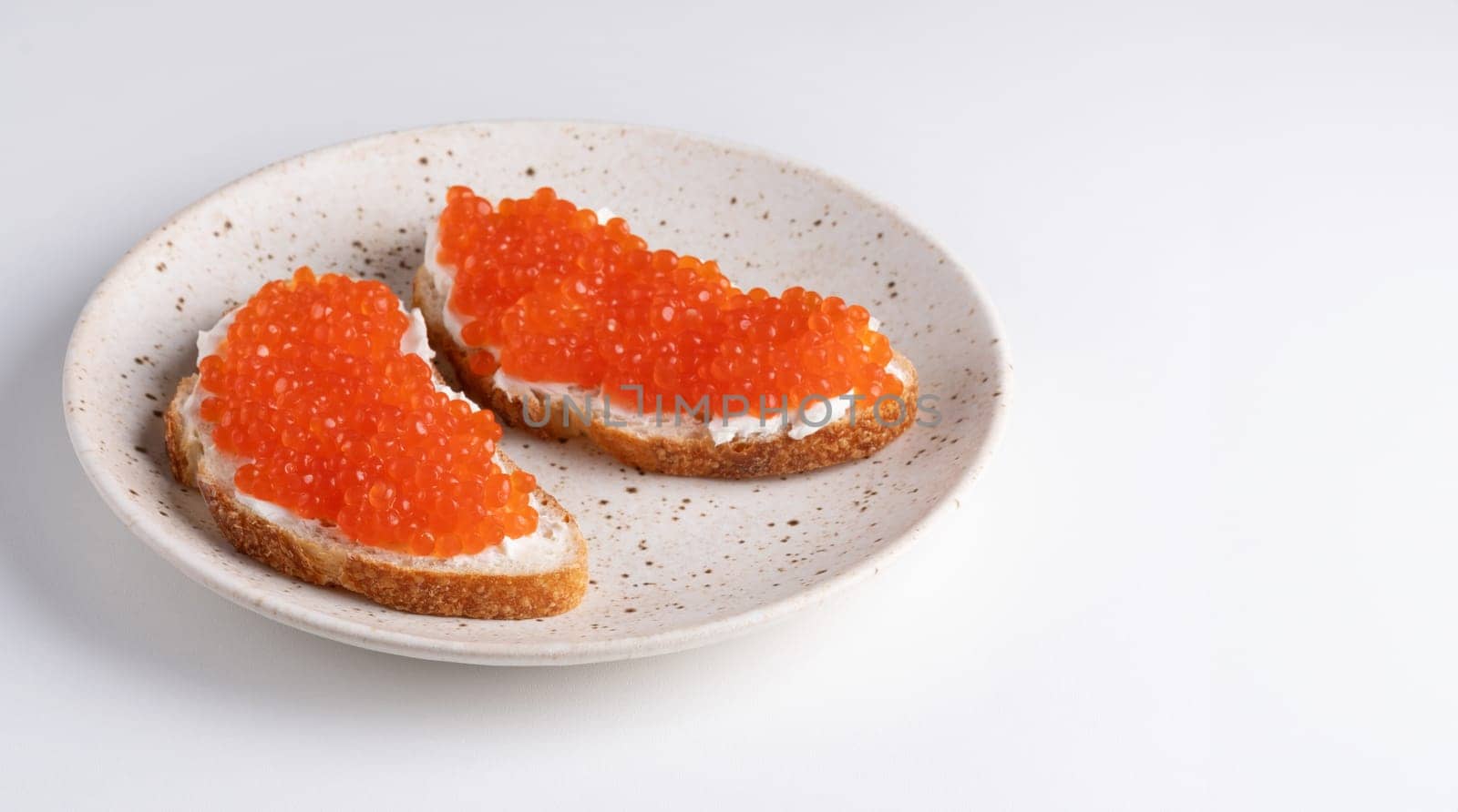 Two sandwiches with red caviar on a plate. A delicious appetizer of trout caviar on a slice of bread with cream cheese. Salted salmon caviar for fish delicacy concept.