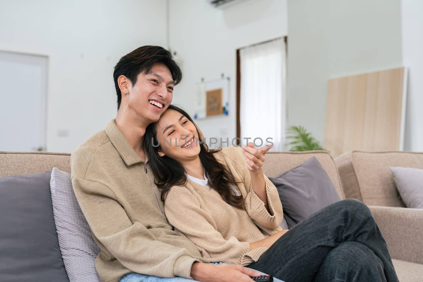 Couple Watches TV together while Sitting on a Couch in the Living Room. Girlfriend and Boyfriend embrace, cuddle, talk, smile and watch Television Streaming Services.