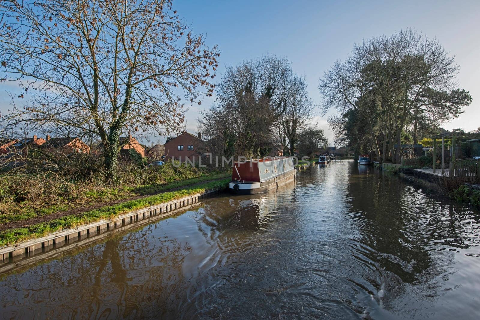 View from a narrowboat travelling in English urban village scenery on British waterway canal with moored boat