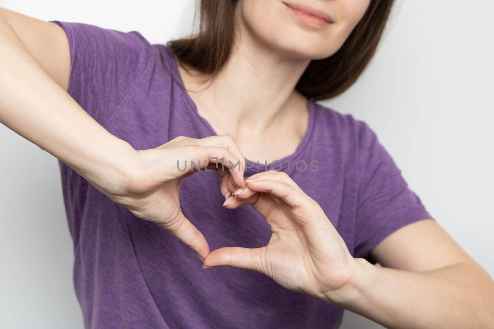 Inspire inclusion. Woman holding her hands in the shape of a heart and holding them in front of her, dressed purple t-shirt. International women's day concept. by Ri6ka
