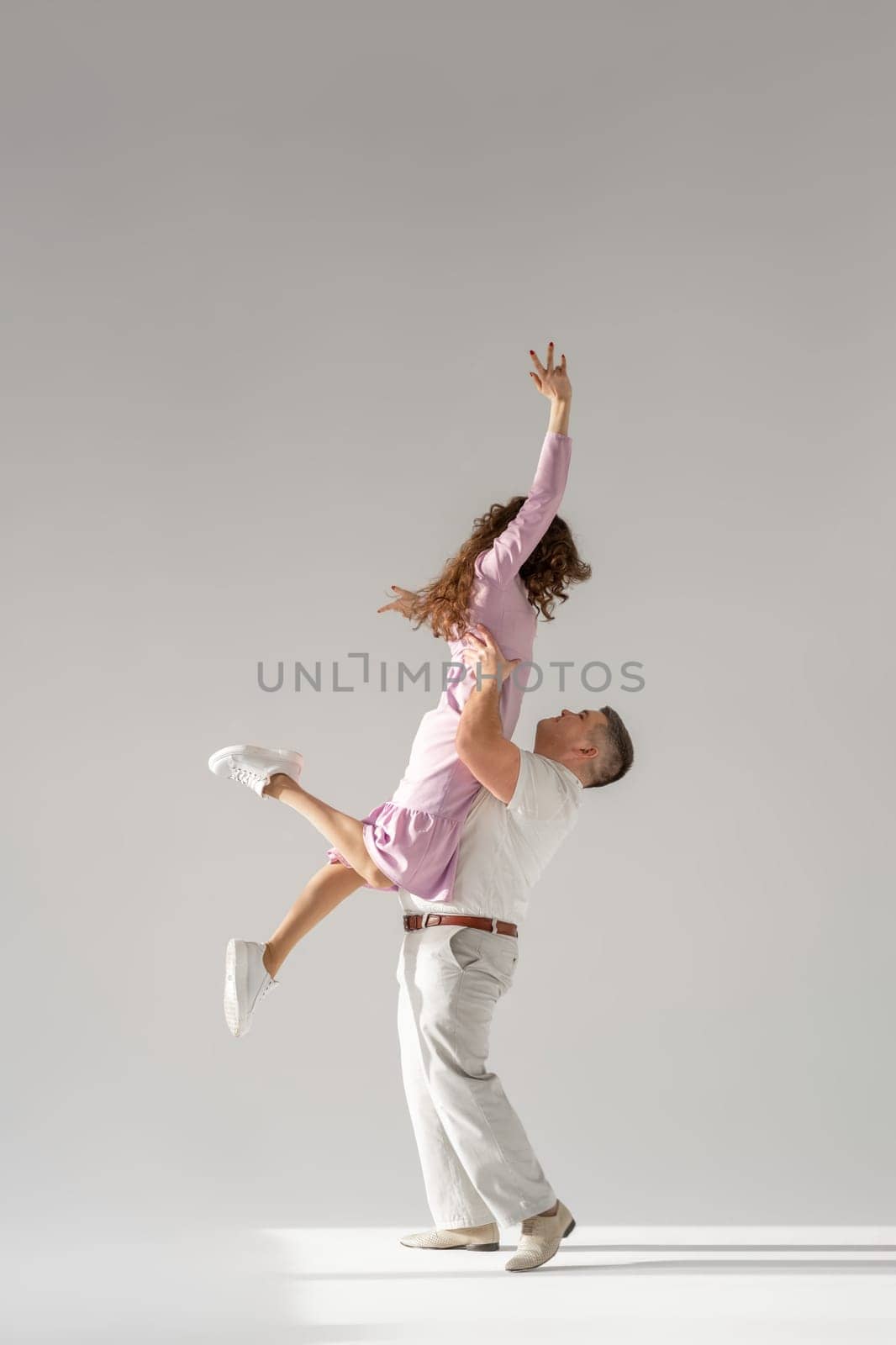 Beautiful young couple dancing on light background. Full length of young beautiful couple bonding while standing against white background