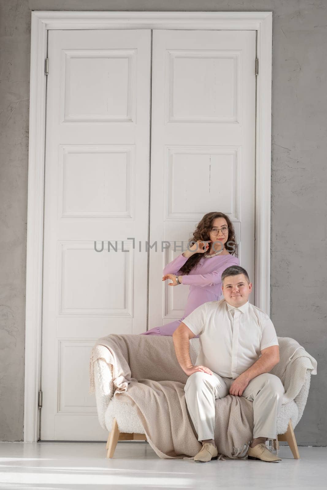 Young happy couple sitting on a sofa in a large studio. Behind them is a large white door. Loving married couple. Cope space for text