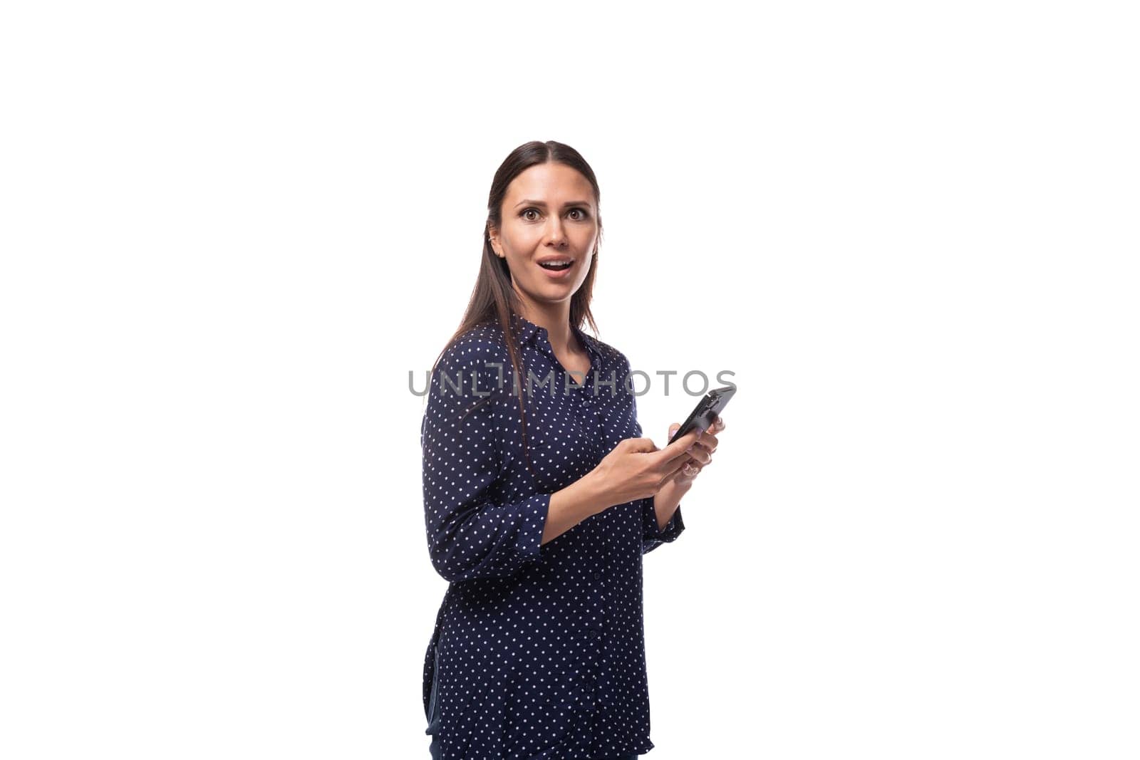 young brunette advertiser woman dressed in blue blouse with polka dots pattern uses smartphone.