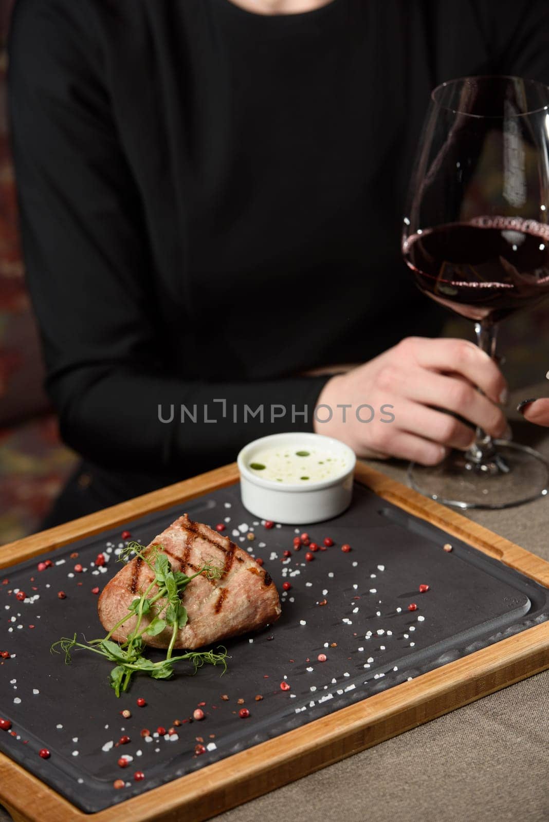 Woman sitting at a table in a restaurant. He is holding a glass of red wine and eating a steak by Ashtray25