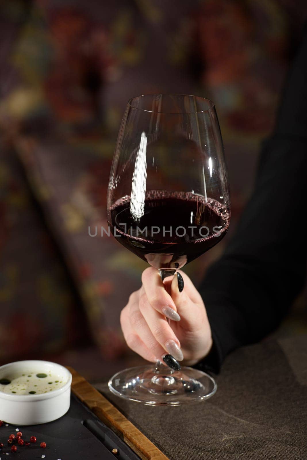 woman sitting at a table in a restaurant. He is holding a glass of red wine and eating a steak.