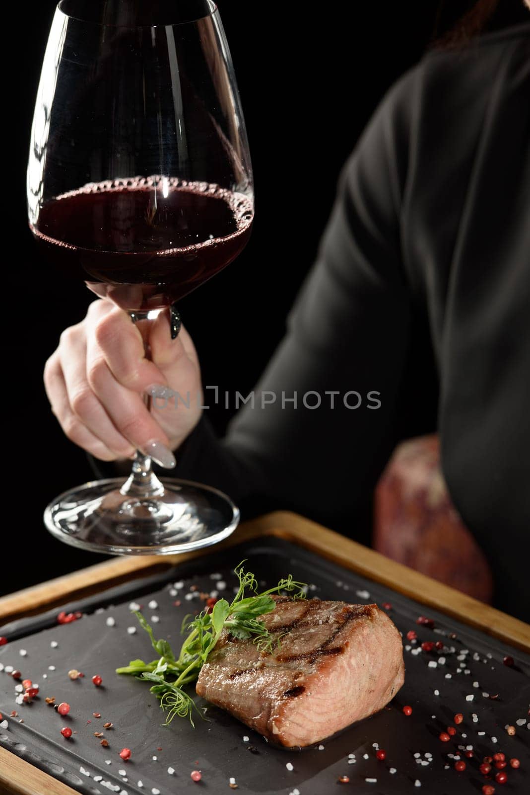 woman sitting at a table in a restaurant. He is holding a glass of red wine and eating a steak.
