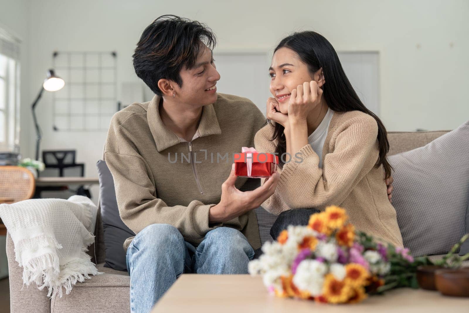 Romantic young asian couple embracing giving present in living room at home. Fall in love. Valentine concept.