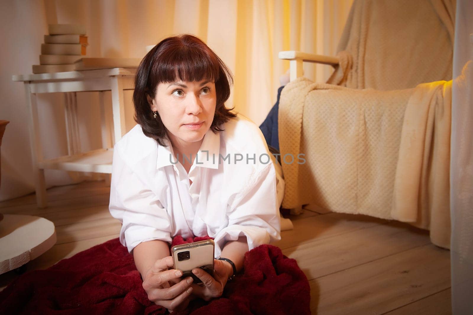 Pretty young woman is using phone in evening cozy room. Attractive girl chatting in living room alone. Modern evening pastime. A blogger with smartphone