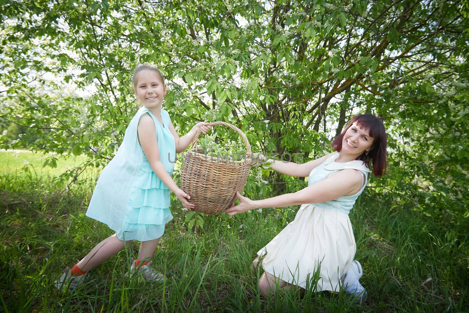 Happy mother and daughter enjoying rest, playing and fun on nature on a green lawn and with a blooming apple tree in the background. Woman and girl resting outdoors in summer and spring day by keleny