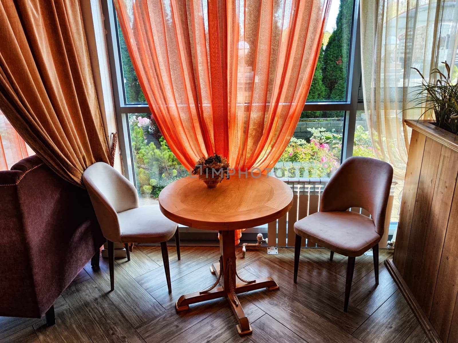 A table in a small cozy cafe or restaurant with window and curtains. Dimmed lights, beautiful Design of the hall. Nobody to a place to relax and eat