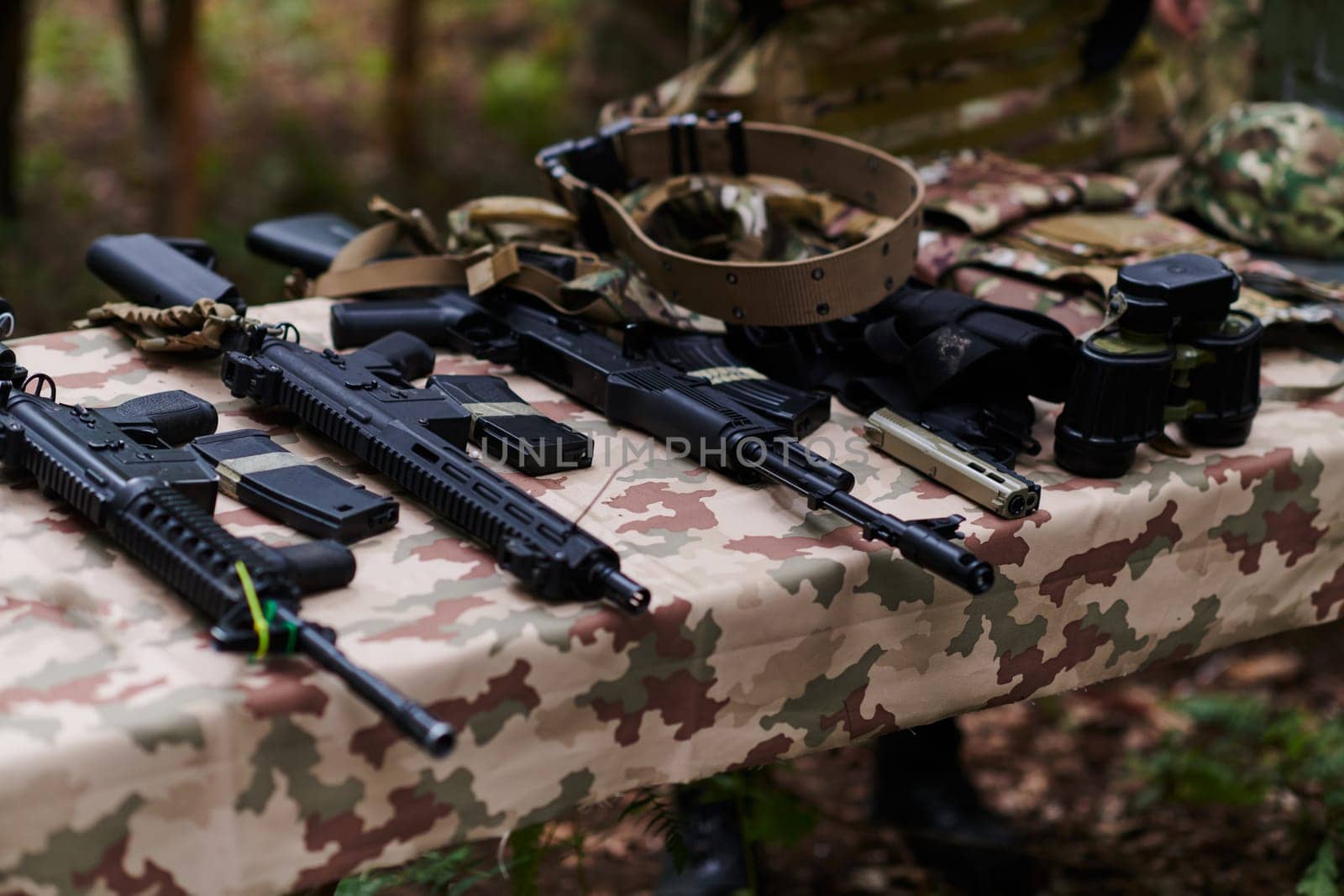 An array of military weapons, including rifles and pistols, is meticulously arranged on a table in a military base, presenting a close-up view of the diverse firepower and armament meticulously organized for readiness and strategic deployment.