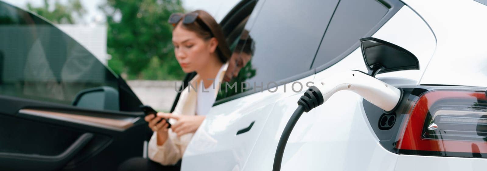 Young woman use smartphone to pay for electricity for EV car. Expedient by biancoblue