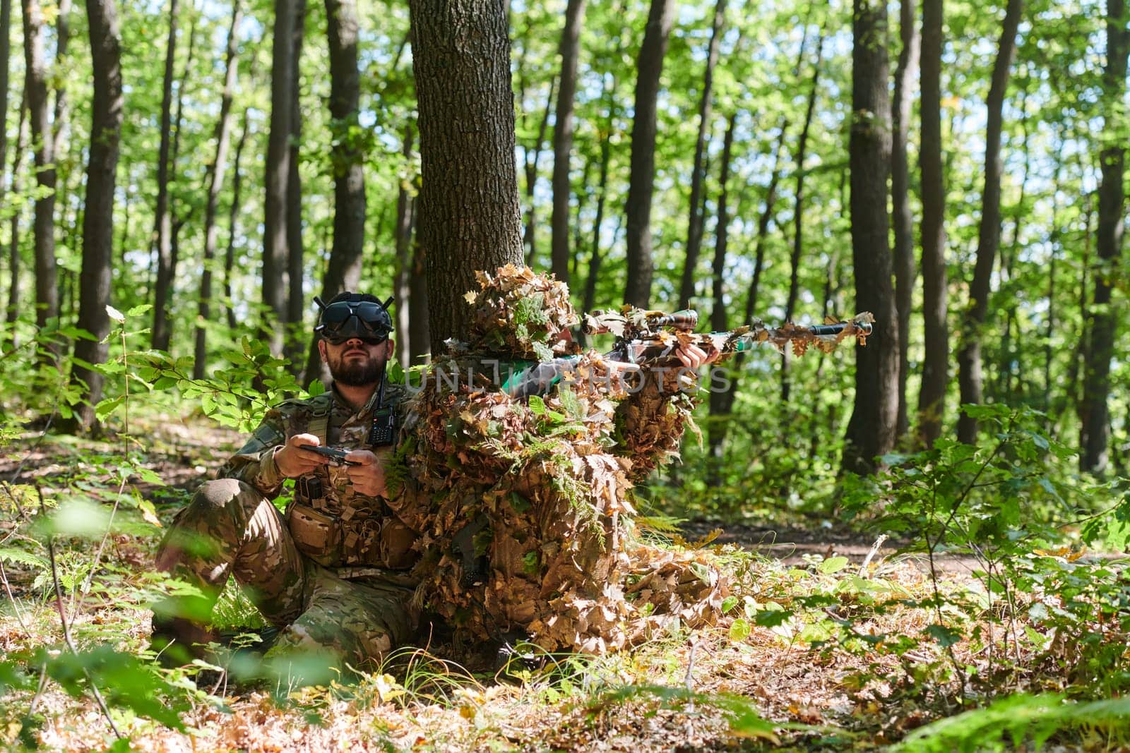 A skilled sniper and a soldier operating a drone with VR goggles strategize and observe the military action while concealed in the forest.