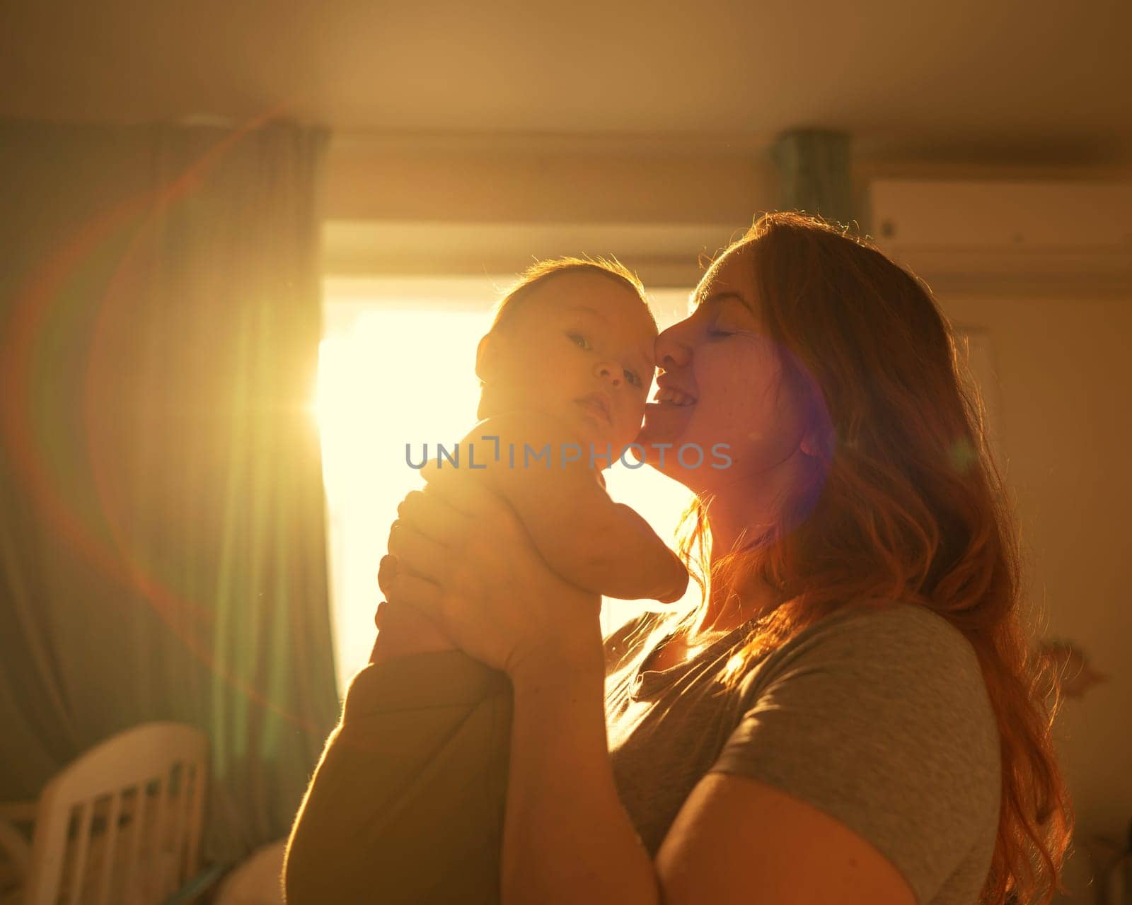 A Caucasian woman tenderly kisses her newborn son in the morning rays of sunlight
