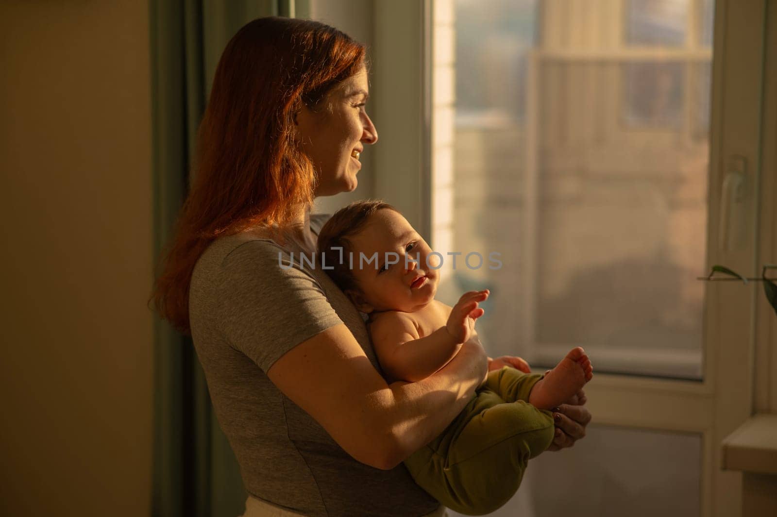 Caucasian woman tenderly holds her newborn son while standing near the window. by mrwed54