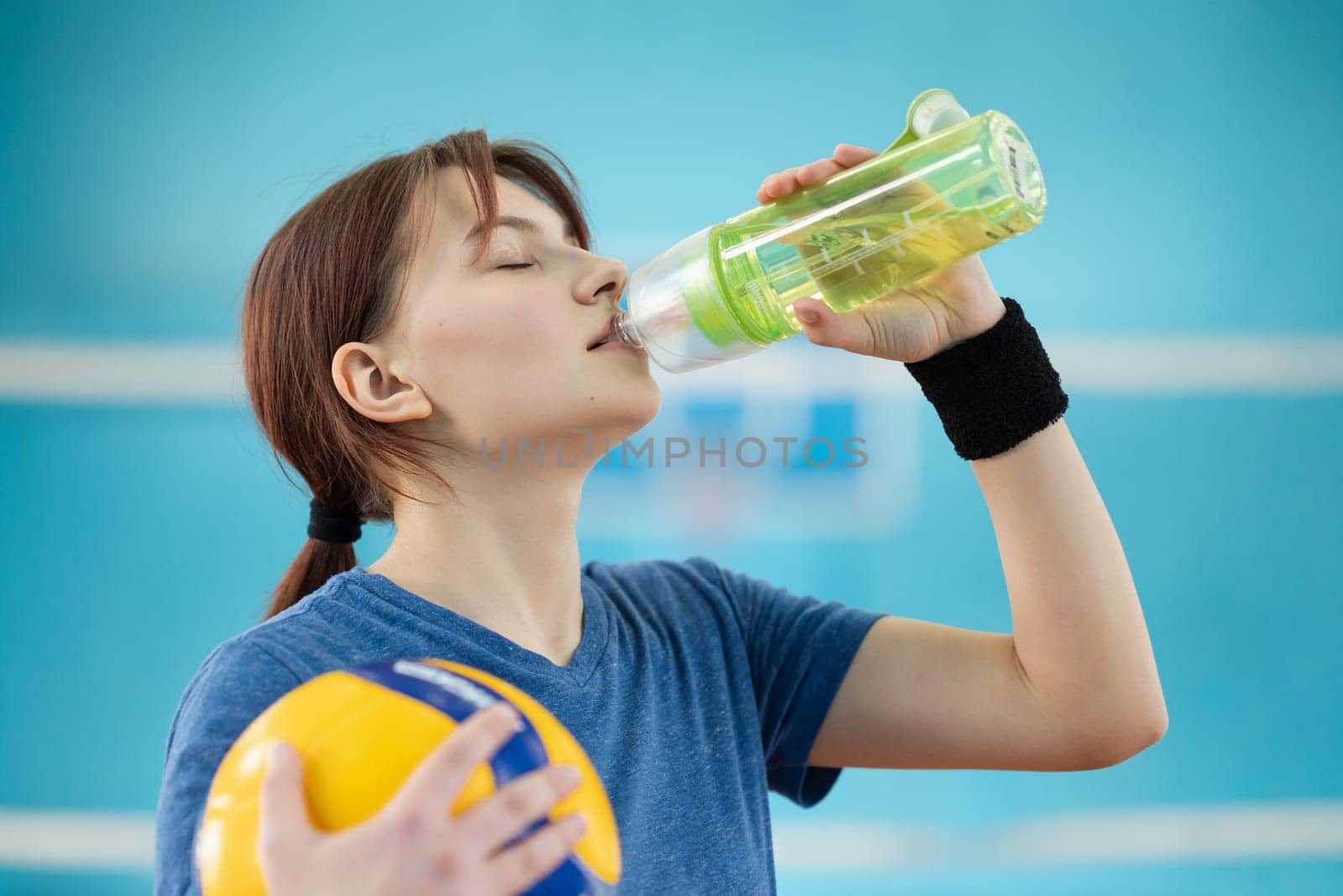 Young girl drinking water while having volleyball training on the court by VitaliiPetrushenko