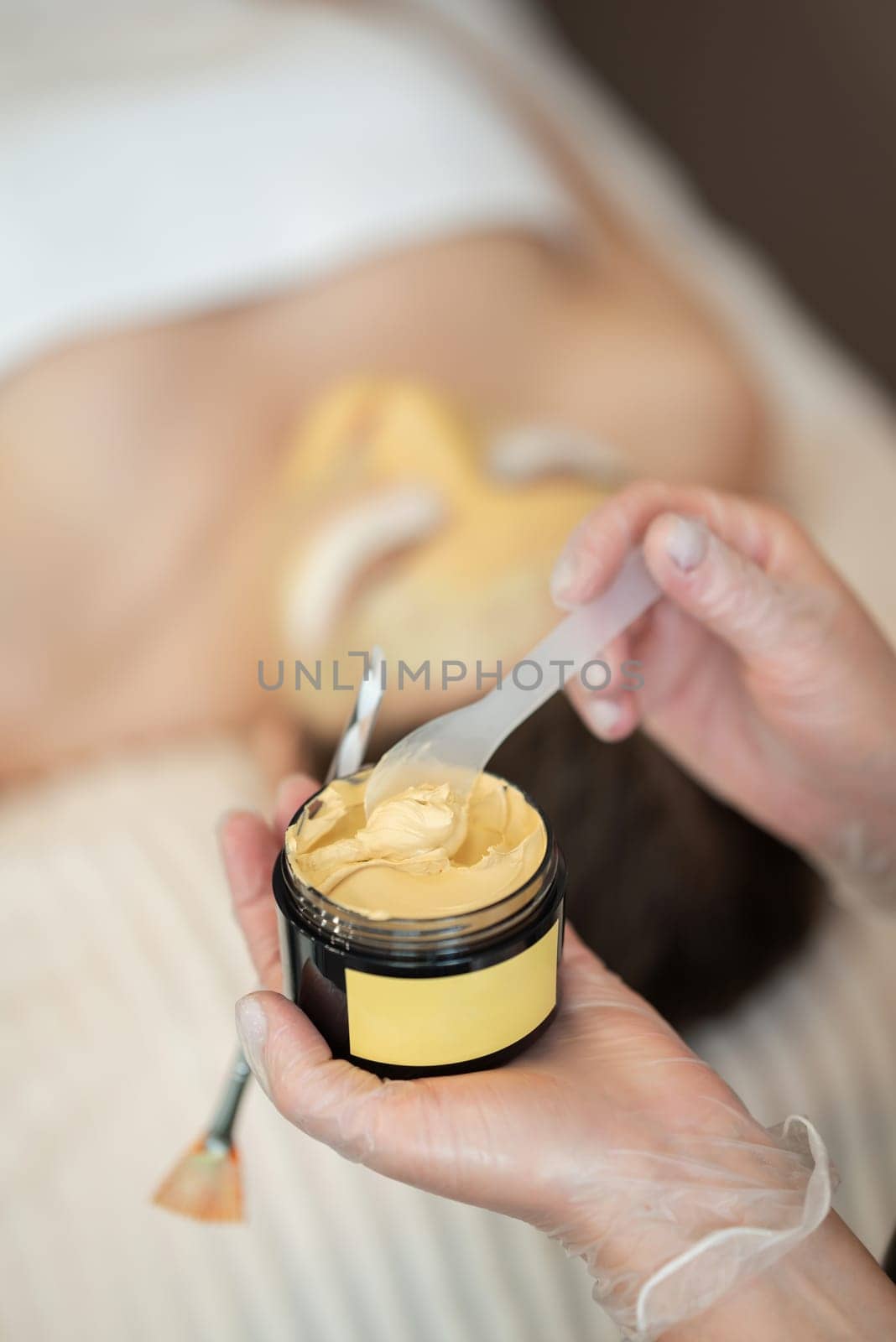 Vertical shot of woman's hands holding a jar with yellow cosmetic mask, close up by VitaliiPetrushenko