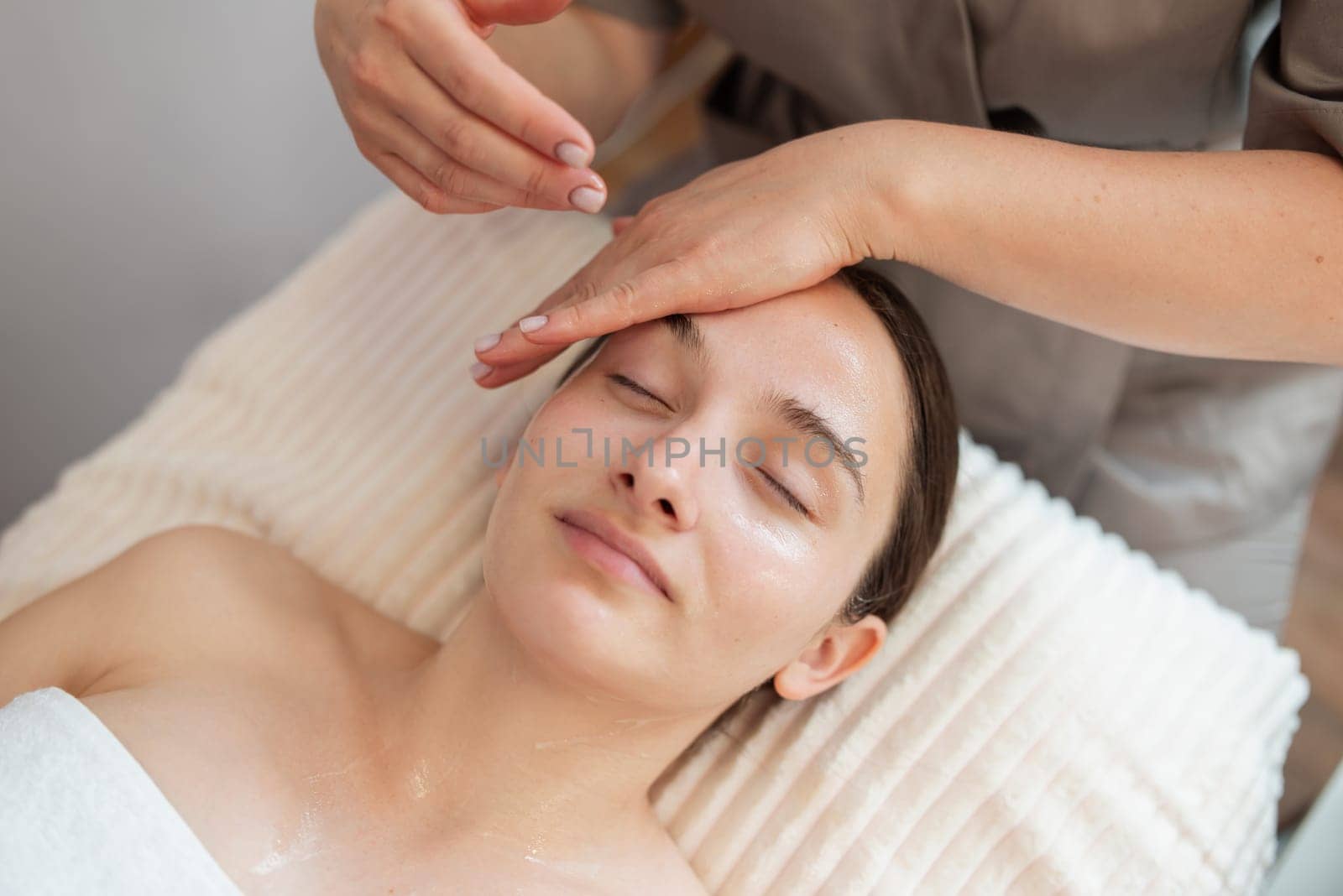 Beautiful young woman enjoying face massage during beauty treatment in the spa, close up by VitaliiPetrushenko