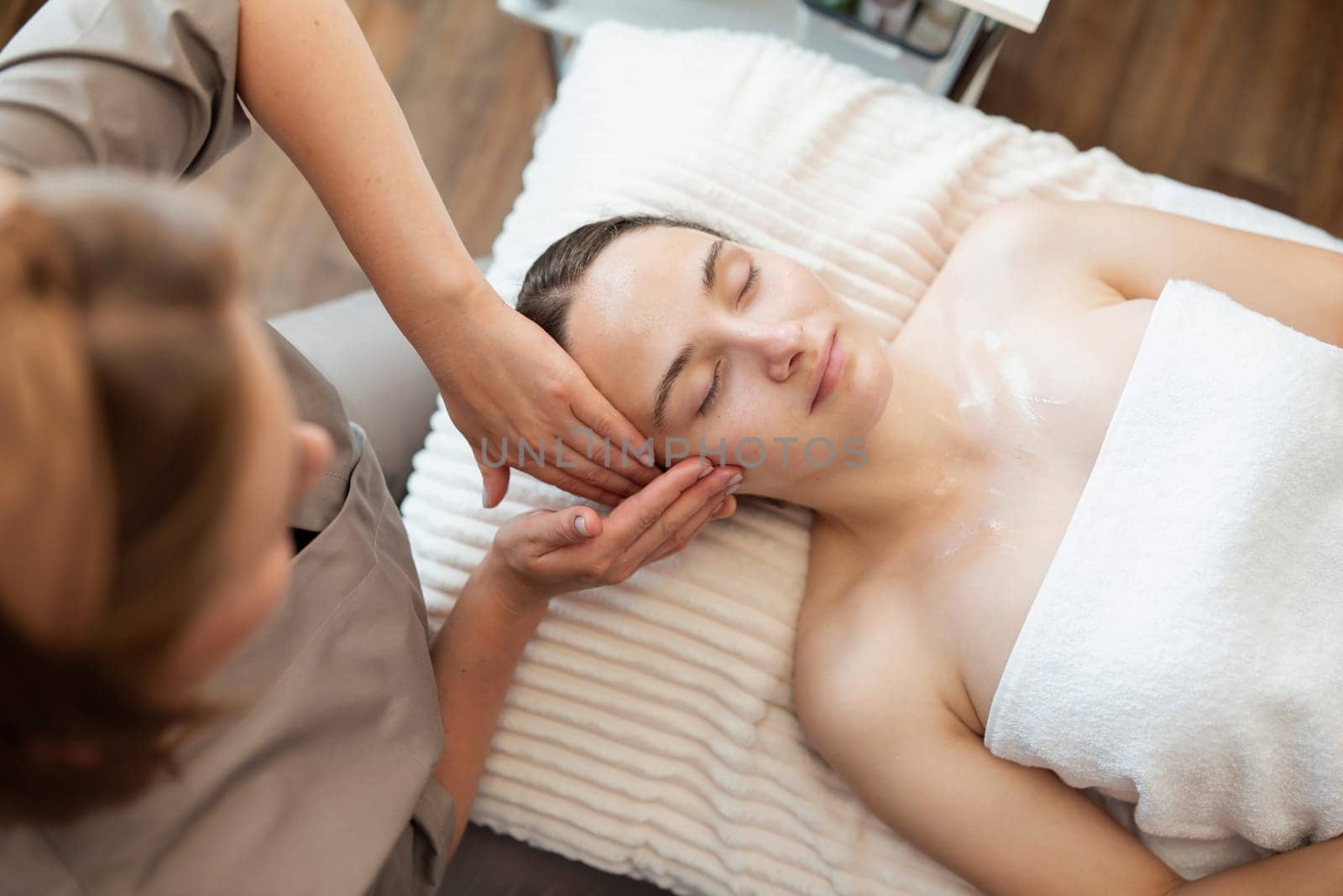 Young girl client of spa salon, lying on the couch while cosmetologist making her a manual facial massage by VitaliiPetrushenko