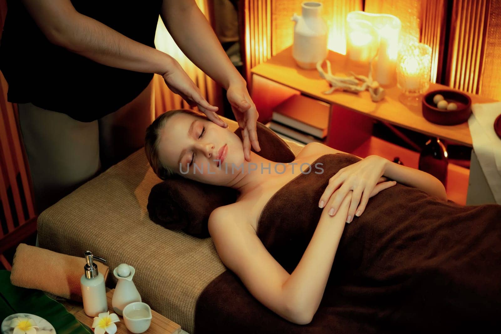 Caucasian woman enjoying relaxing anti-stress head massage and pampering facial beauty skin recreation leisure in warm candle lighting ambient salon spa in luxury resort or hotel. Quiescent