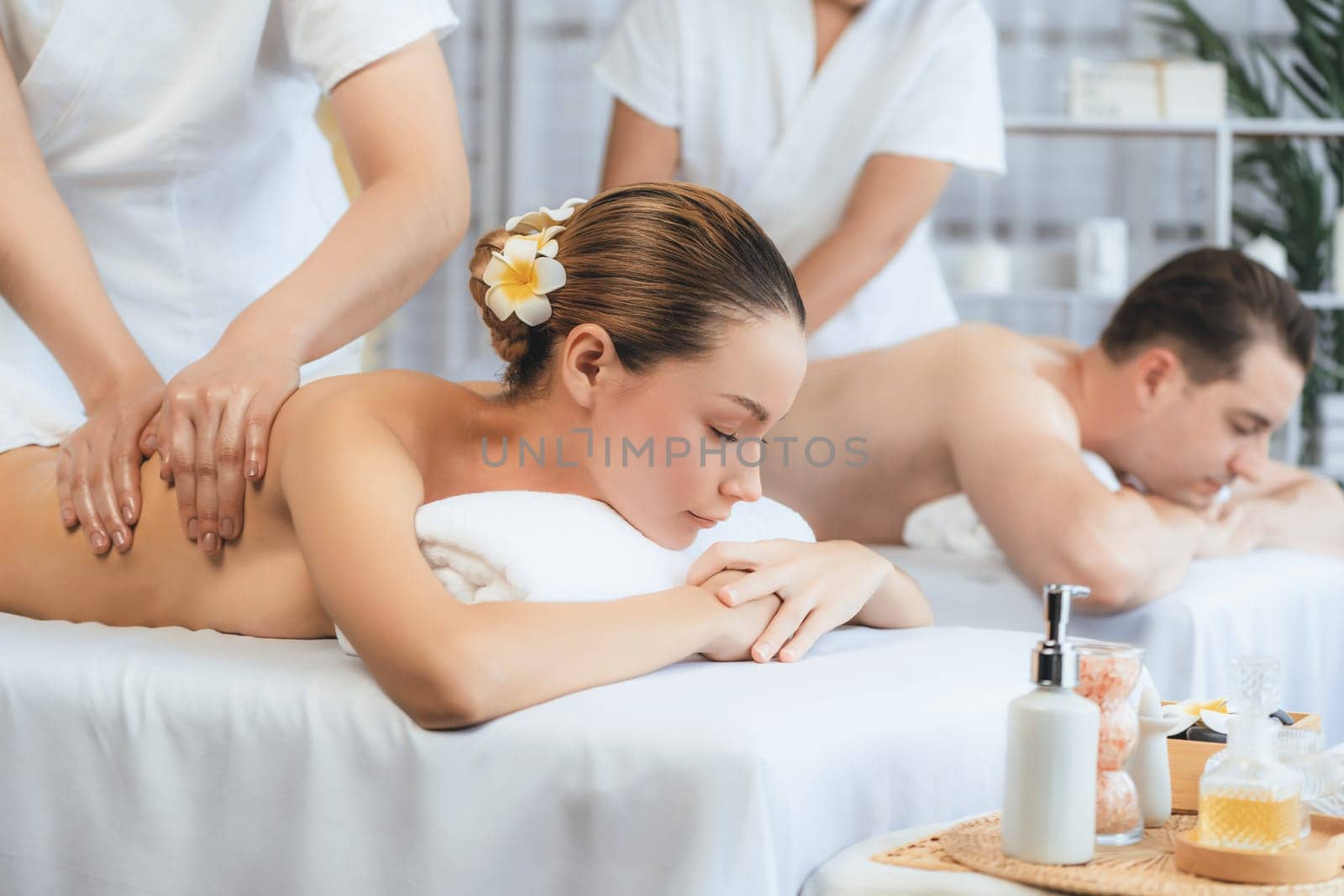 Caucasian couple customer enjoying relaxing anti-stress spa massage and pampering with beauty skin recreation leisure in day light ambient salon spa at luxury resort or hotel. Quiescent