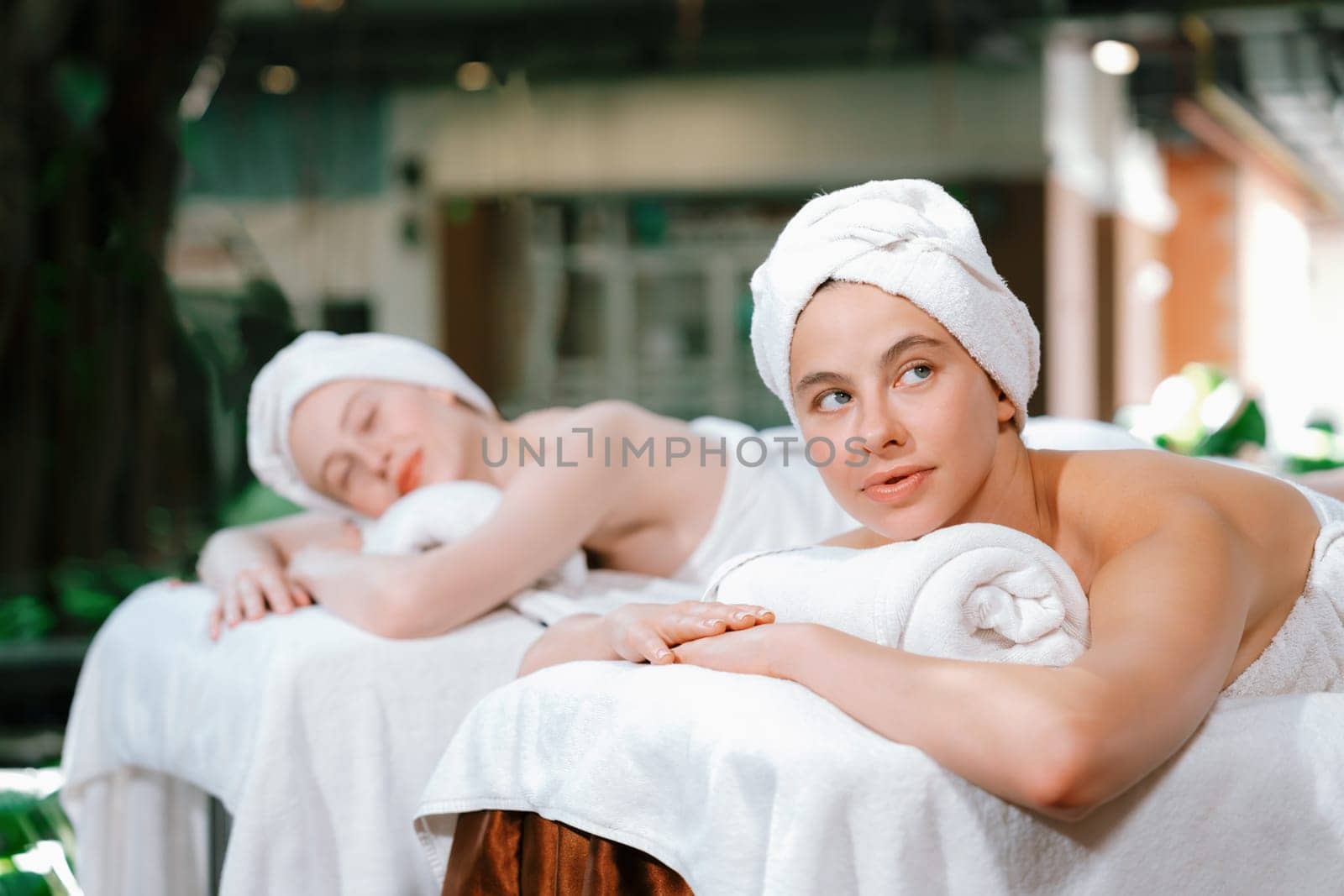 A portrait of a couple of a beautiful young caucasian woman with white towel rest on comfortable spa bed with relaxation while having body massage with professional masseur at spa salon.Tranquility.