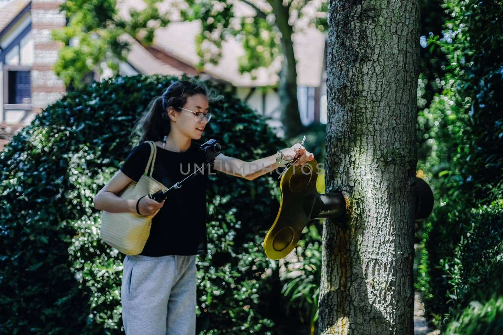 Portrait of one beautiful Caucasian brunette teenage girl with a mini camera on a stick turns a large golden key sticking out of a tree trunk on a sunny summer day, close-up side view.