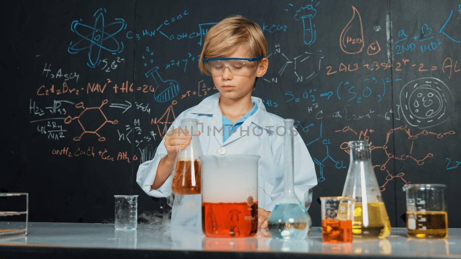 Smart boy inspect mixed chemical liquid in laboratory beakers while holding and looking carefully. Caucasian child focus on doing an experiment in chemistry lesson or STEM science class. Erudition.