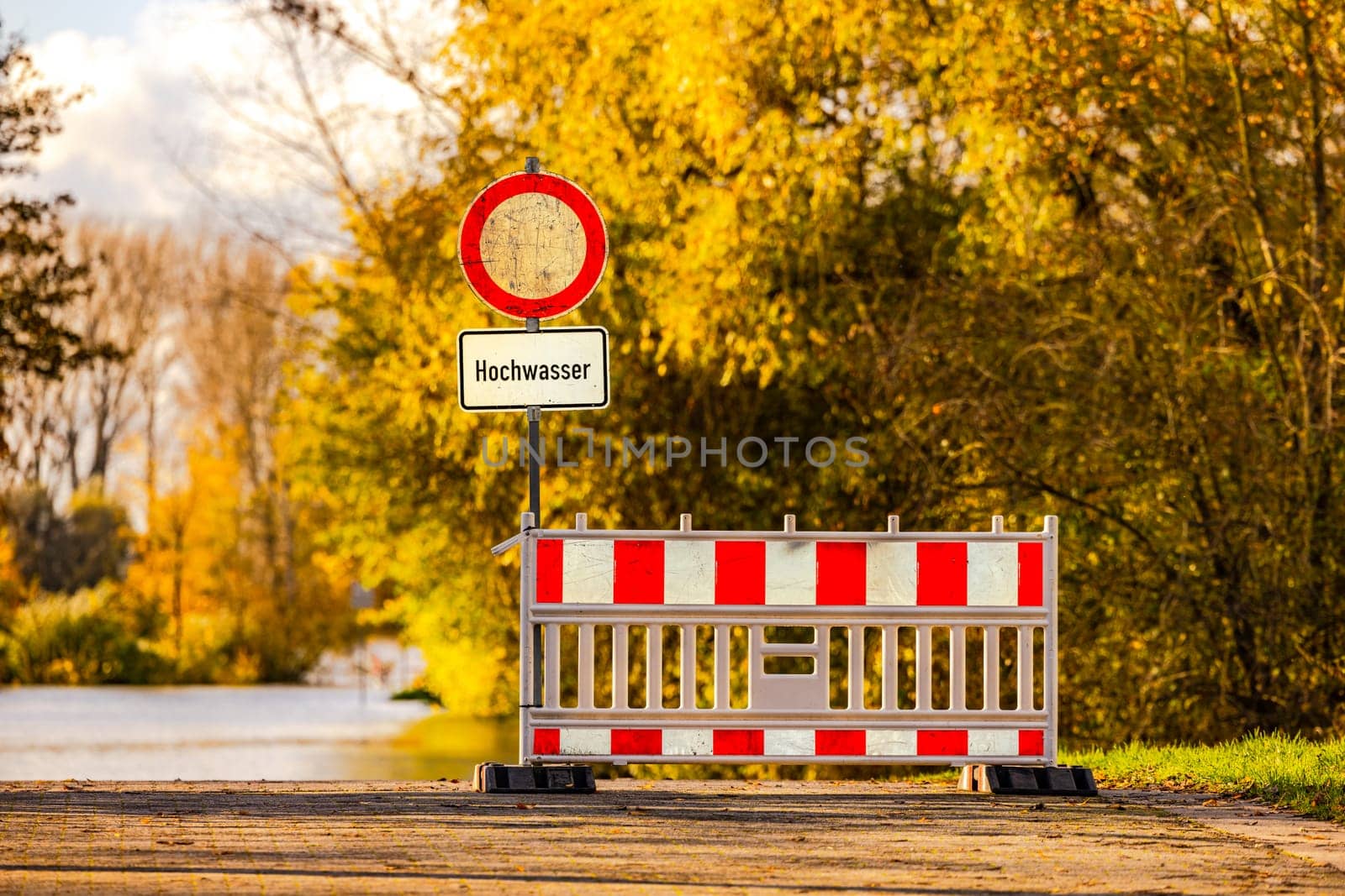Backlight mood in sunshine with warning sign high water on a road on the river Rhine, Germany