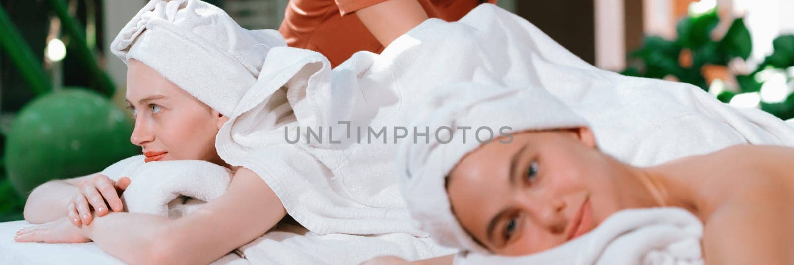 A portrait of a couple of a beautiful young caucasian woman with white towel rest on comfortable spa bed with relaxation while having body massage with professional masseur at spa salon.Tranquility.