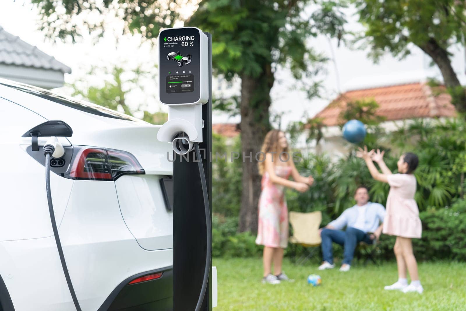 Focus EV station recharging battery for EV car on blurred family. Synchronos by biancoblue