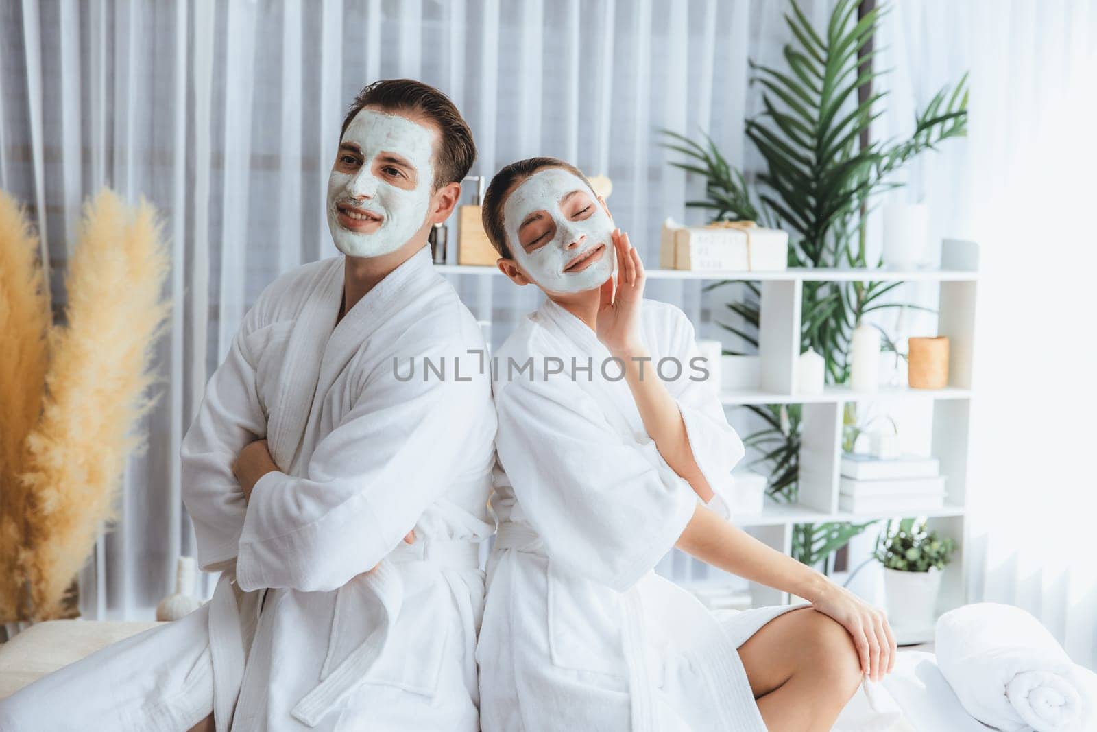 Blissful couple in bathrobe with facial cream mask enjoying serene ambiance of spa salon resort or hotel during holiday. Pampering face spa and skincare treatment with essence relaxation. Quiescent