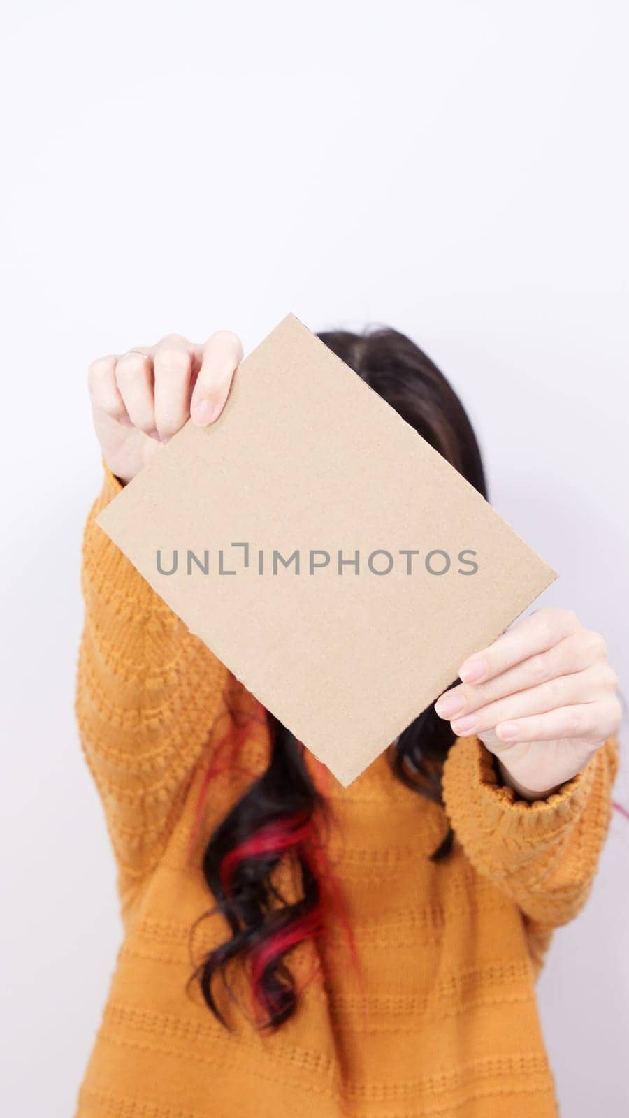 Beautiful young smiling brunette woman in yellow sweater holding blank placard with Copy Space for advertisement. Selective focus, vertical. Empty billboard with space for text over white background
