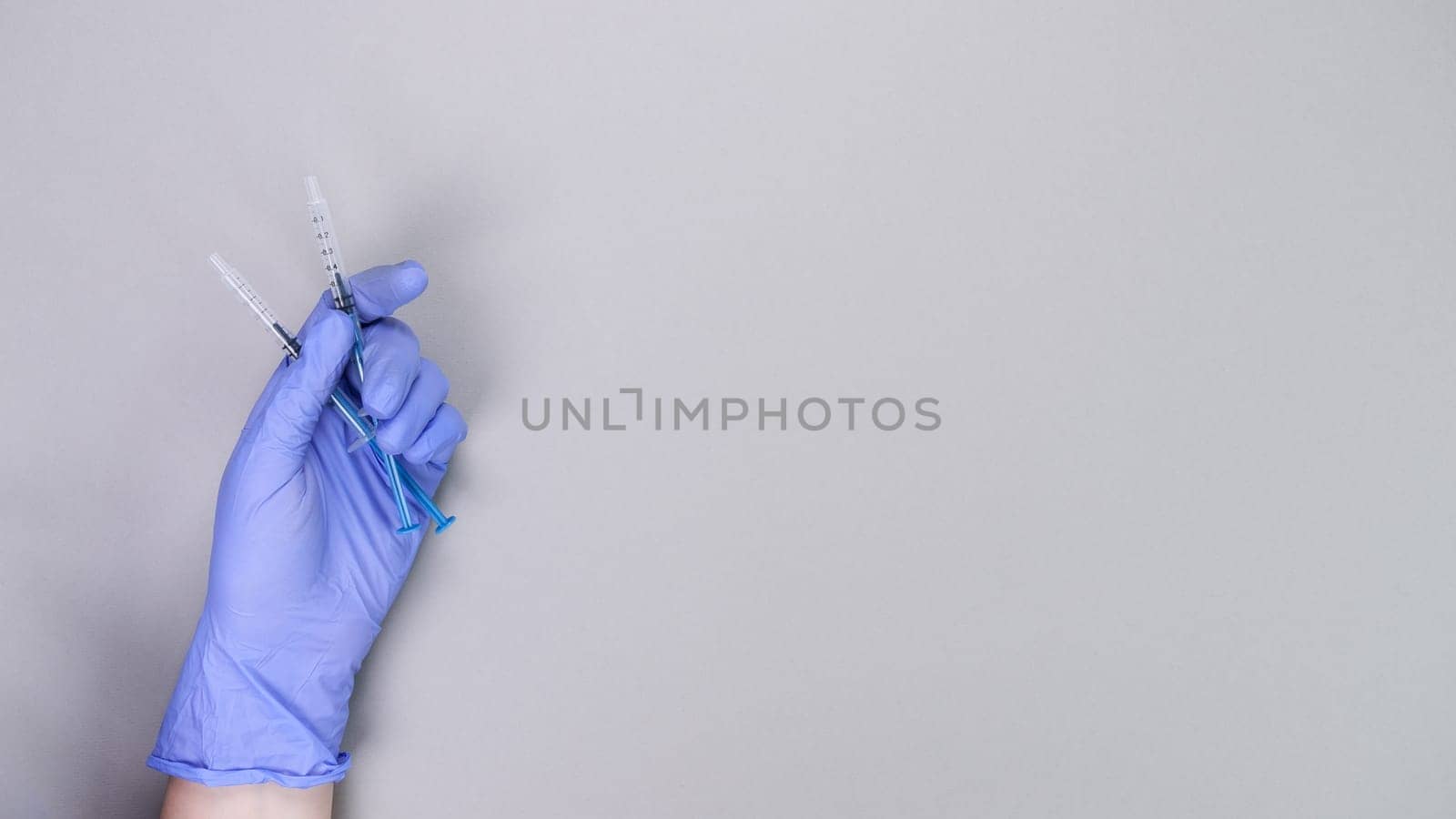 Hand in blue gloves of doctor or nurse holding syringe with liquid vaccine over grey background with copy space. New vaccine. Unknown vaccine. Medical gloves. by JuliaDorian