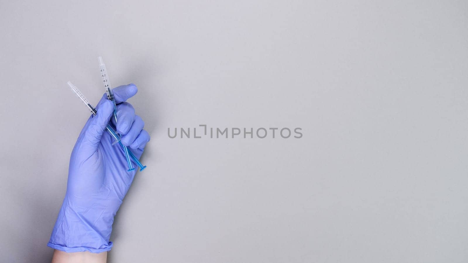 Hand in blue gloves of doctor or nurse holding syringe with liquid vaccine over grey background with copy space. New vaccine. Unknown vaccine. Medical gloves