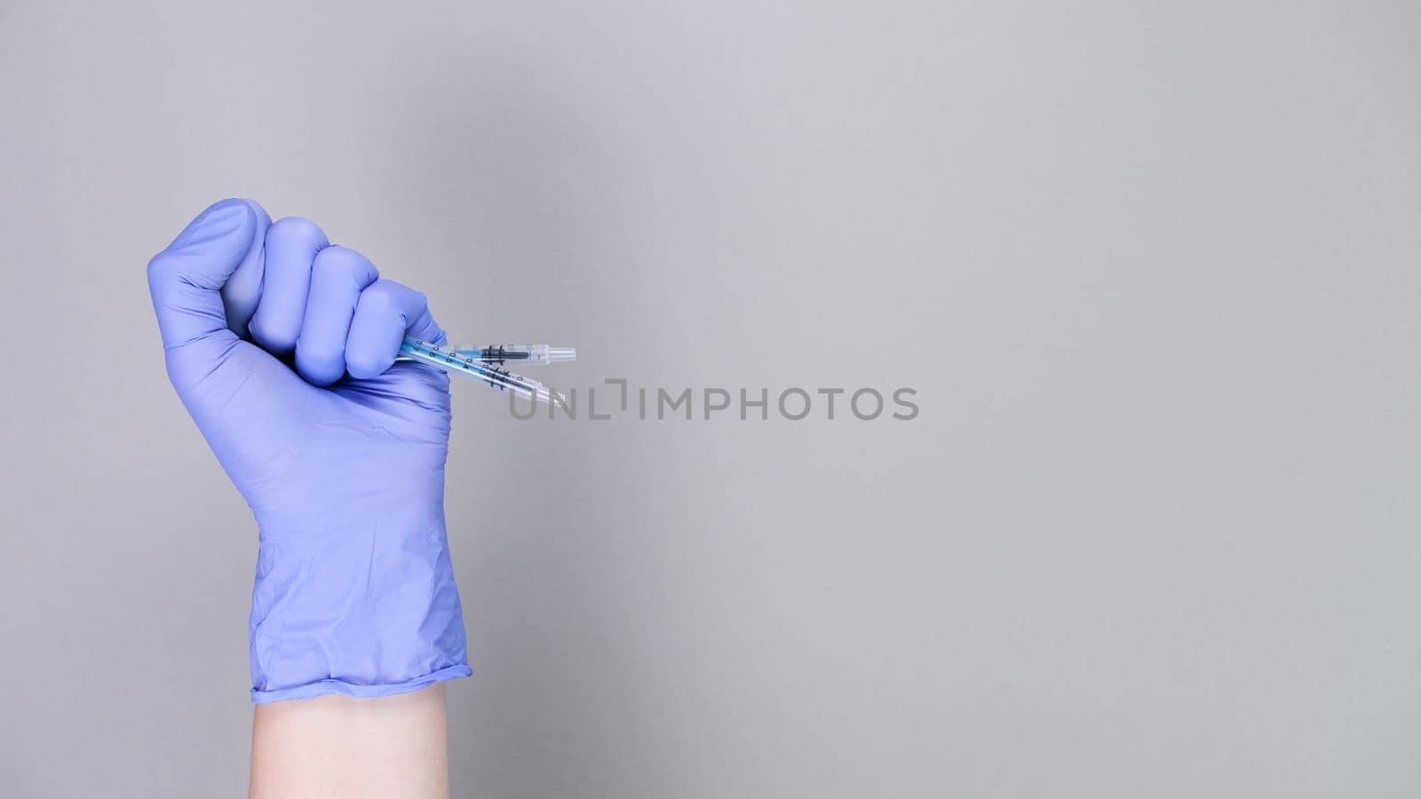 Hand in blue gloves of doctor or nurse holding syringe with liquid vaccine over grey background with copy space. New vaccine. Unknown vaccine. Medical gloves