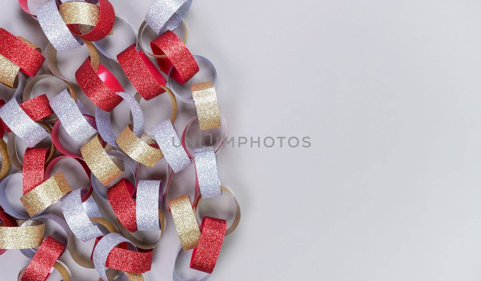 Colorful background with strips of gold silver red sparkling chain garland on grey. Festive Christmas birthday decoration garland.Space for text. by JuliaDorian