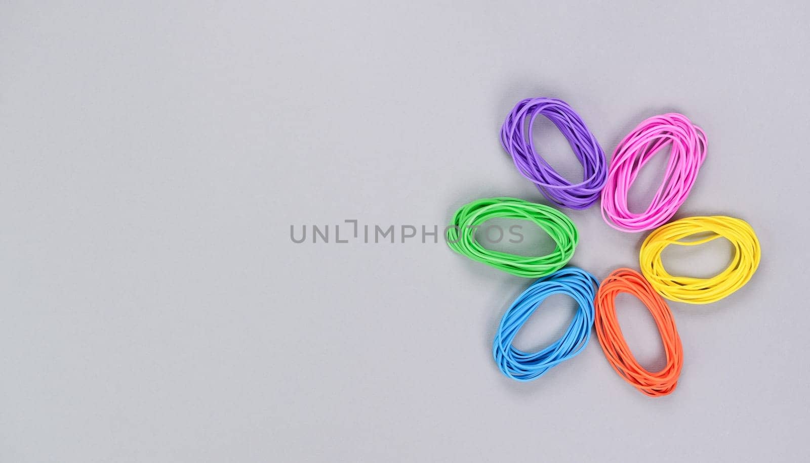 Multicolored flower made of elastic. Top view of colorful rubber bands isolated on grey. Rainbow elastic rubber bands on white. Rainbow flower shape. by JuliaDorian