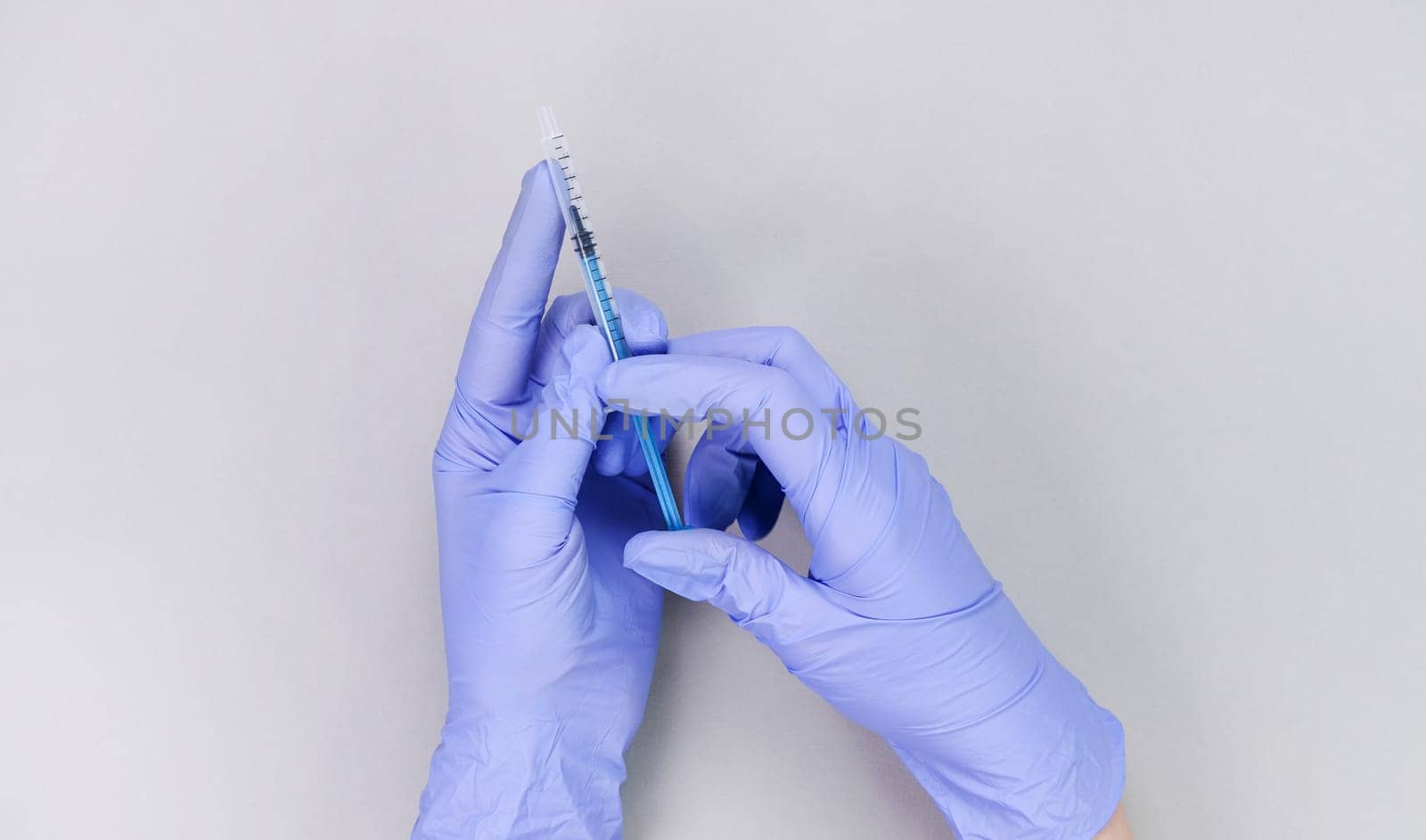 Hands in blue gloves of doctor or nurse holding syringe with liquid vaccine over grey background with copy space. New vaccine. Unknown vaccine. Medical gloves