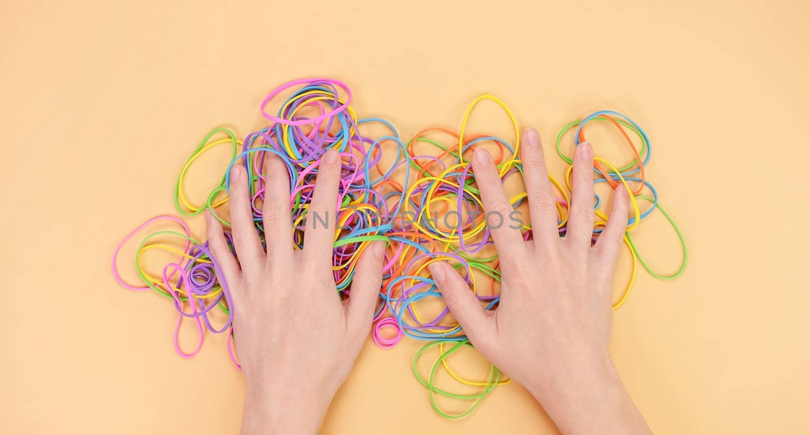 Hands hiding colored rubber bands for money on bright yellow paper background. Abstract background. Stationery accessories. by JuliaDorian