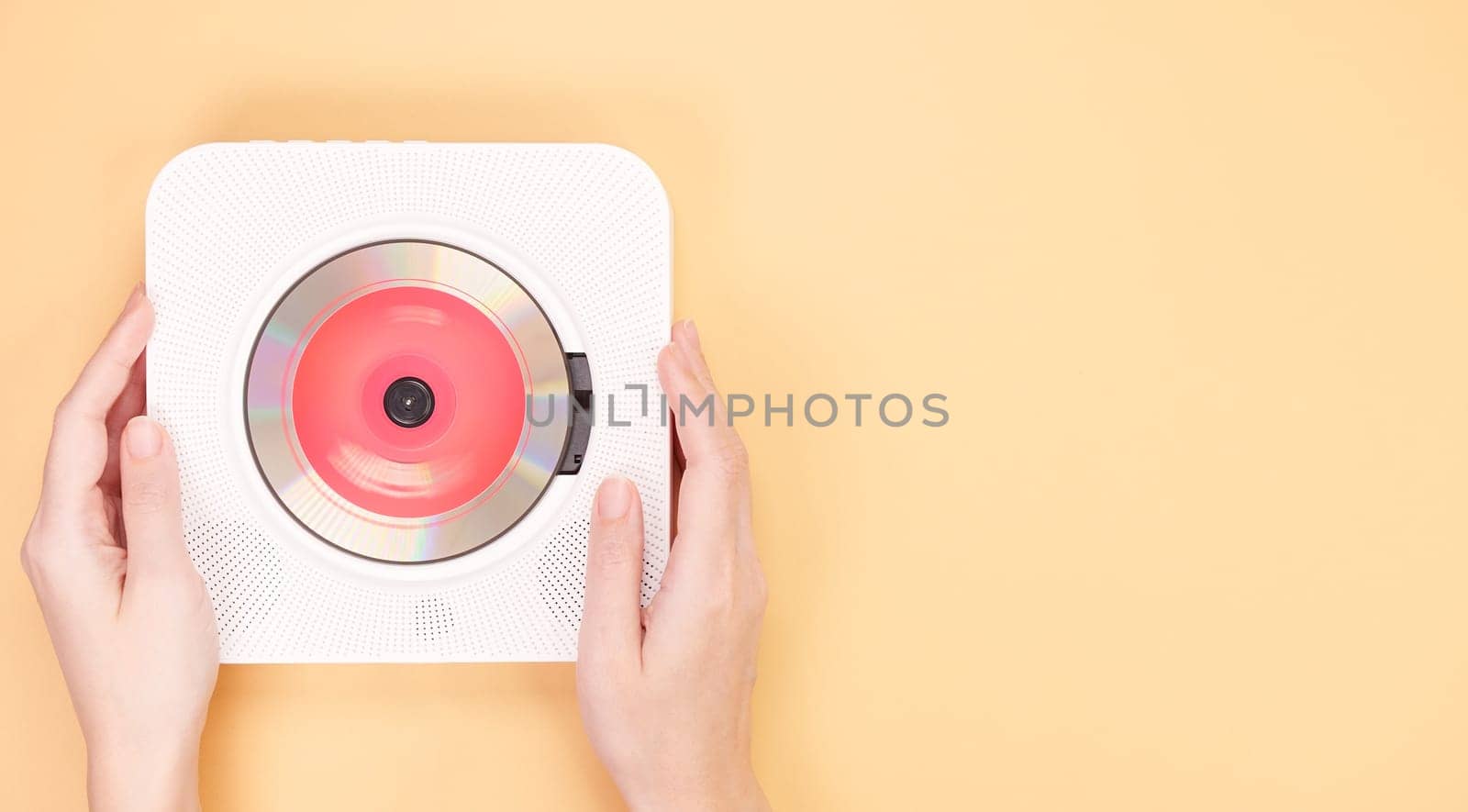 Hands holding stylish white portable compact CD player with red cd disc playing music on yellow background. Retro vintage trending disc player. Top view, space for text. Hobby entertainment leisure.