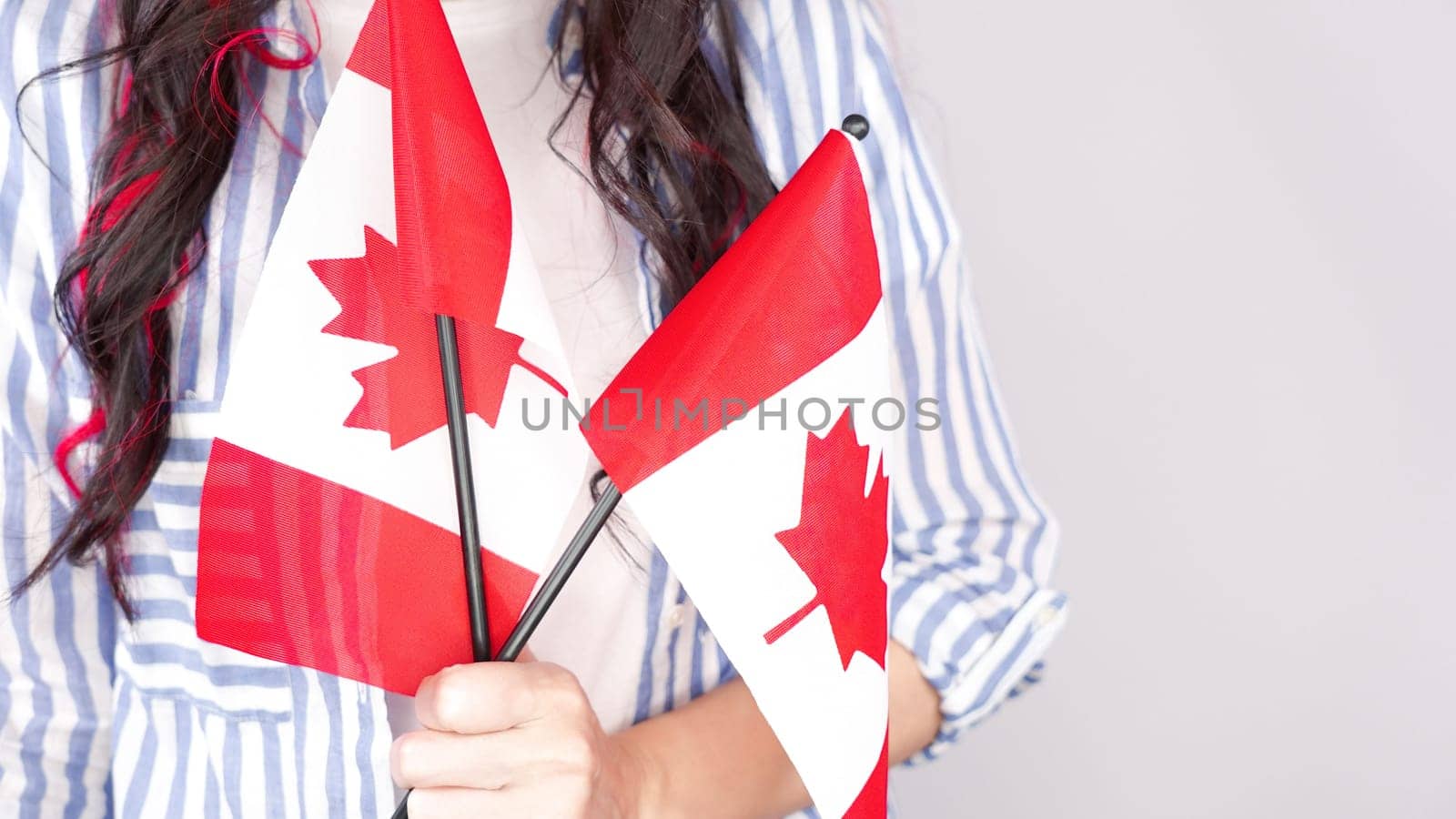 Unrecognized girl student in white blue shirt holding small canadian flag over gray background, Canada day, holiday, vote, immigration, tax, copy space.